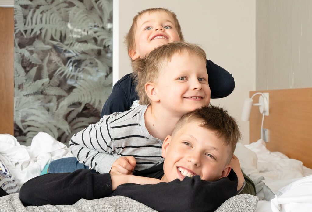 Kolme poikaa makaavat sängyllä päällekkäin ja nauravat.