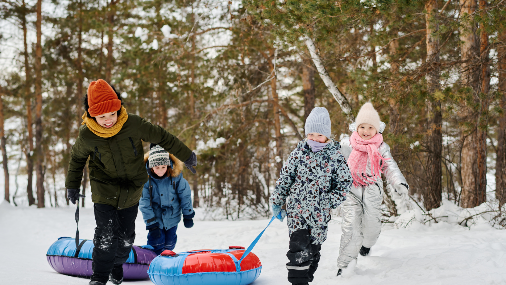 Lapset leikkivät lumisessa metsässä ja vetävät värikkäitä liukurenkaita mäkeä ylös talvipäivänä.